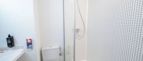 Un baño con un inodoro blanco, una ducha con puerta de vidrio y pared de azulejos.