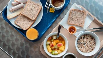 A tray with sandwiches, a bowl of fruit, a bowl of cereal, and a cup of tea.