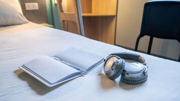 Una cama bien hecha con un cuaderno y auriculares encima.