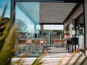 Un patio moderno al aire libre con paredes de vidrio, sillas de metal y una planta en maceta.