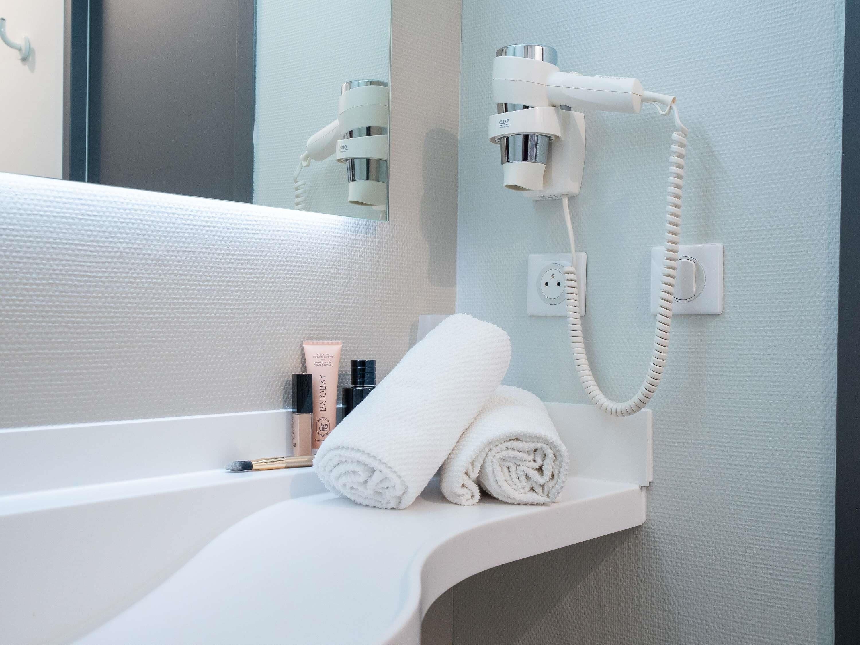 A bathroom with a white bathtub, a towel, and a hairdryer mounted on the wall.