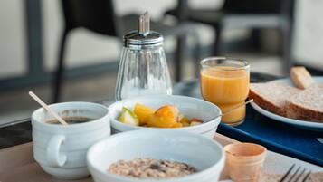 A breakfast tray with a glass of orange juice, a bowl of fruit, a bowl of cereal, a salt shaker, and a small cup.