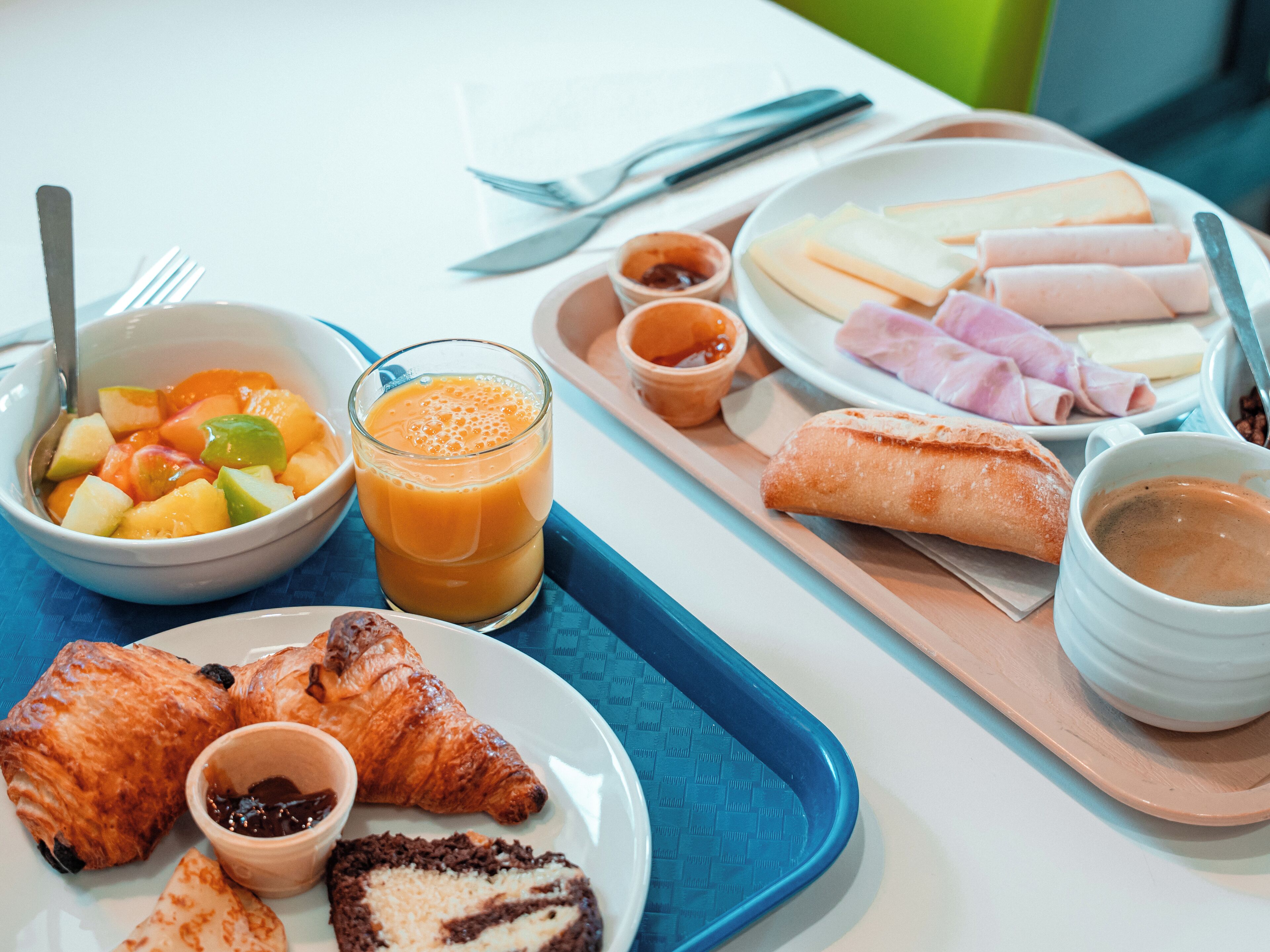 Una bandeja de desayuno con cruasanes, un bol de fruta, jugo, queso, jamón y café.