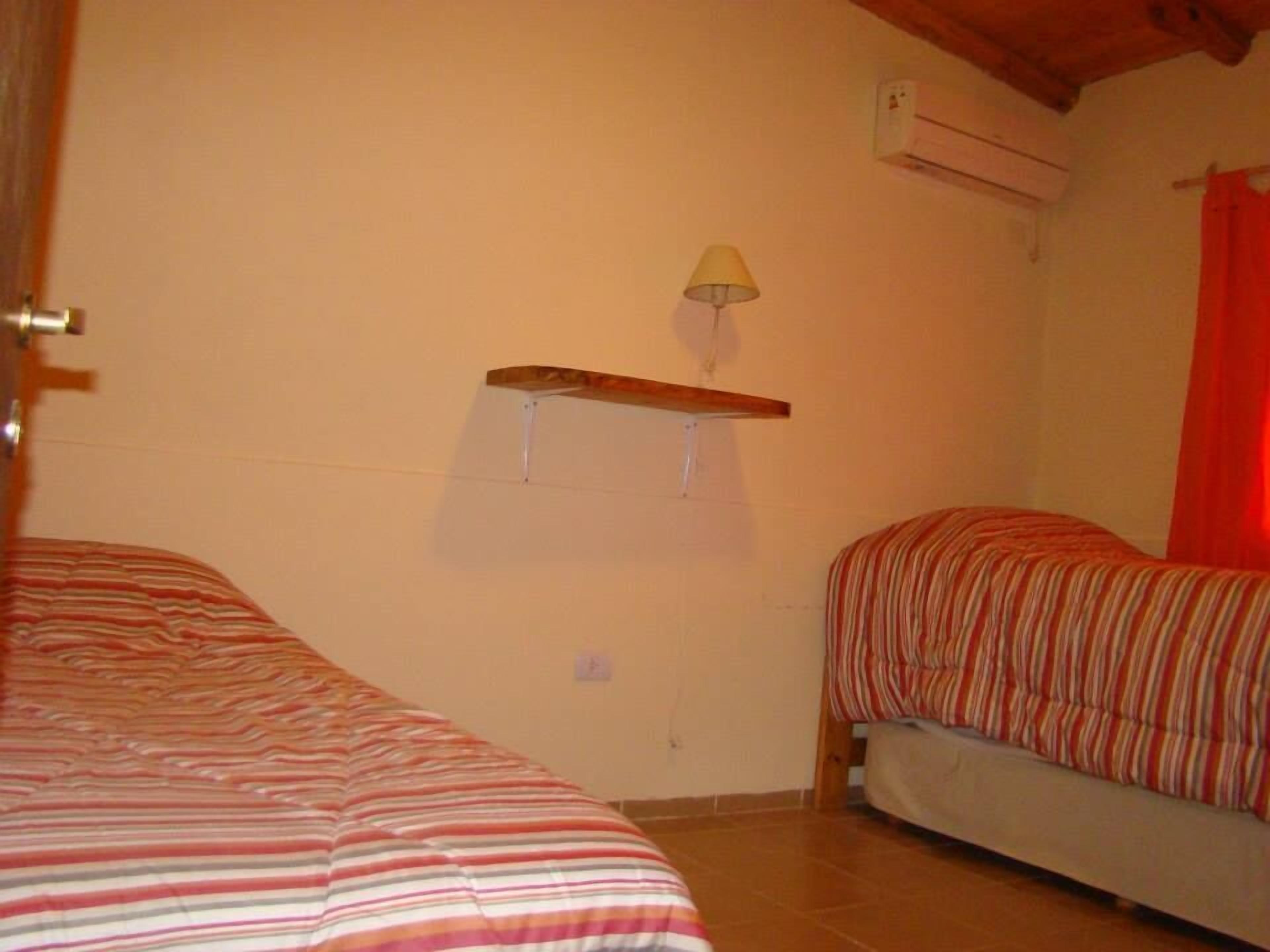 A bedroom with two beds, a wall-mounted shelf with a lamp, and an air conditioning unit.