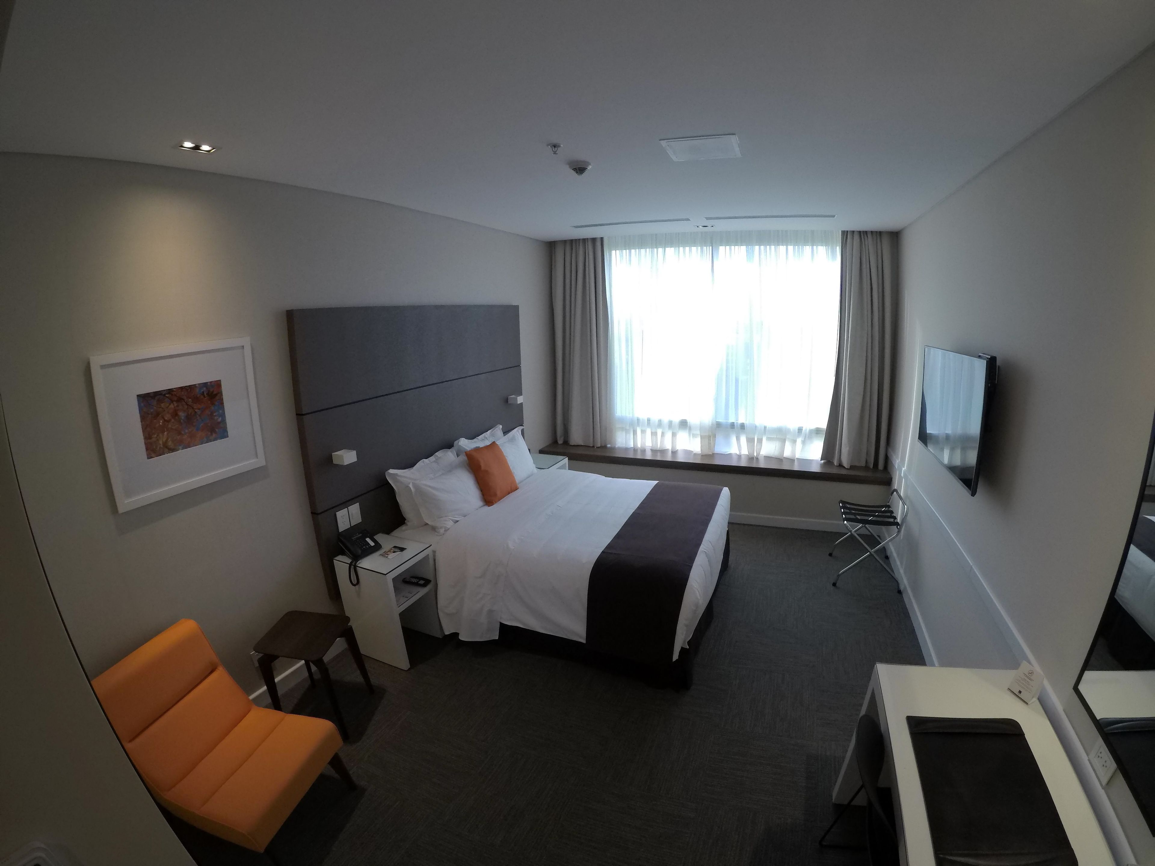 A hotel room with a large bed, a desk, a chair, a TV, and a window with curtains.