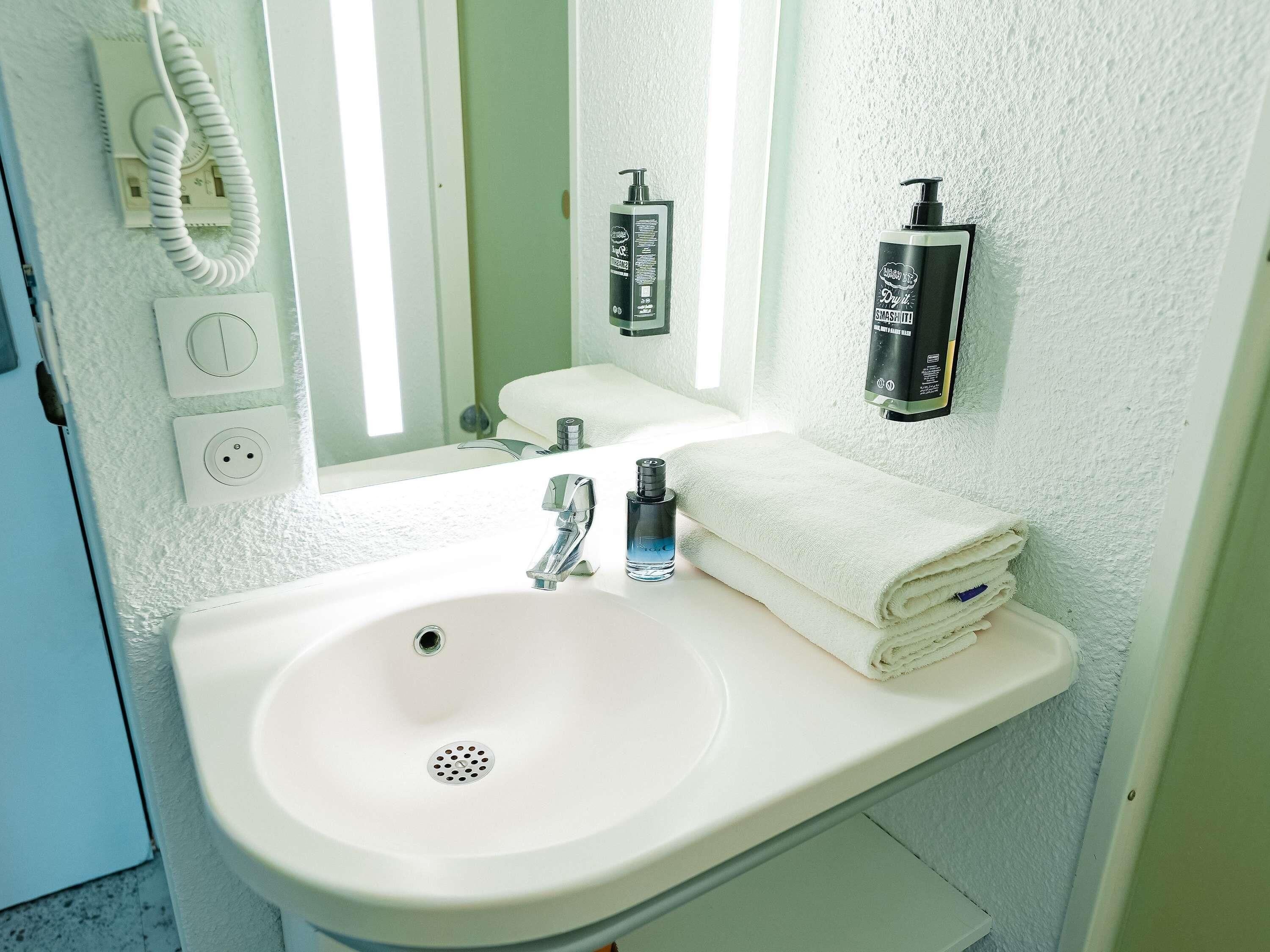 A bathroom with a white sink, a mirror, a towel, and a hand soap dispenser.