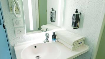 A bathroom with a white sink, a mirror, a towel, and a hand soap dispenser.