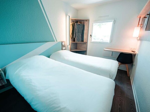 Quarto de hotel com duas camas, uma escrivaninha, um guarda-roupa e uma janela.
