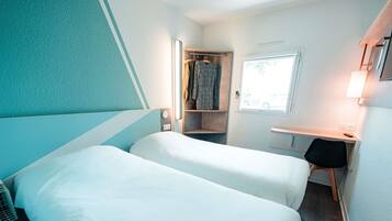A compact hotel room with two beds, a small desk, and a wardrobe.