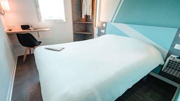 A hotel room with a bed, a desk, a chair, a wardrobe, and a window.