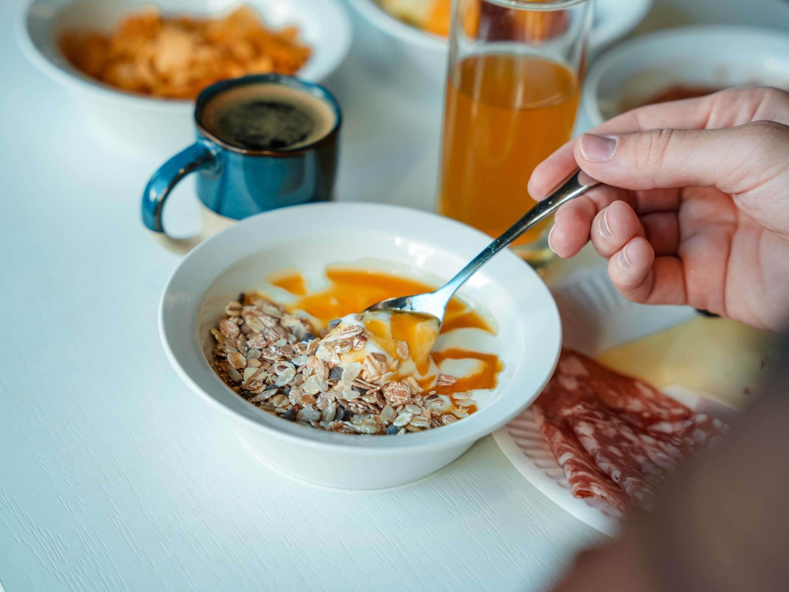 A breakfast setting with a bowl of cereal, a glass of orange juice, and a plate of cured meat.