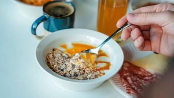 A breakfast setting with a bowl of cereal, a glass of orange juice, and a plate of cured meat.