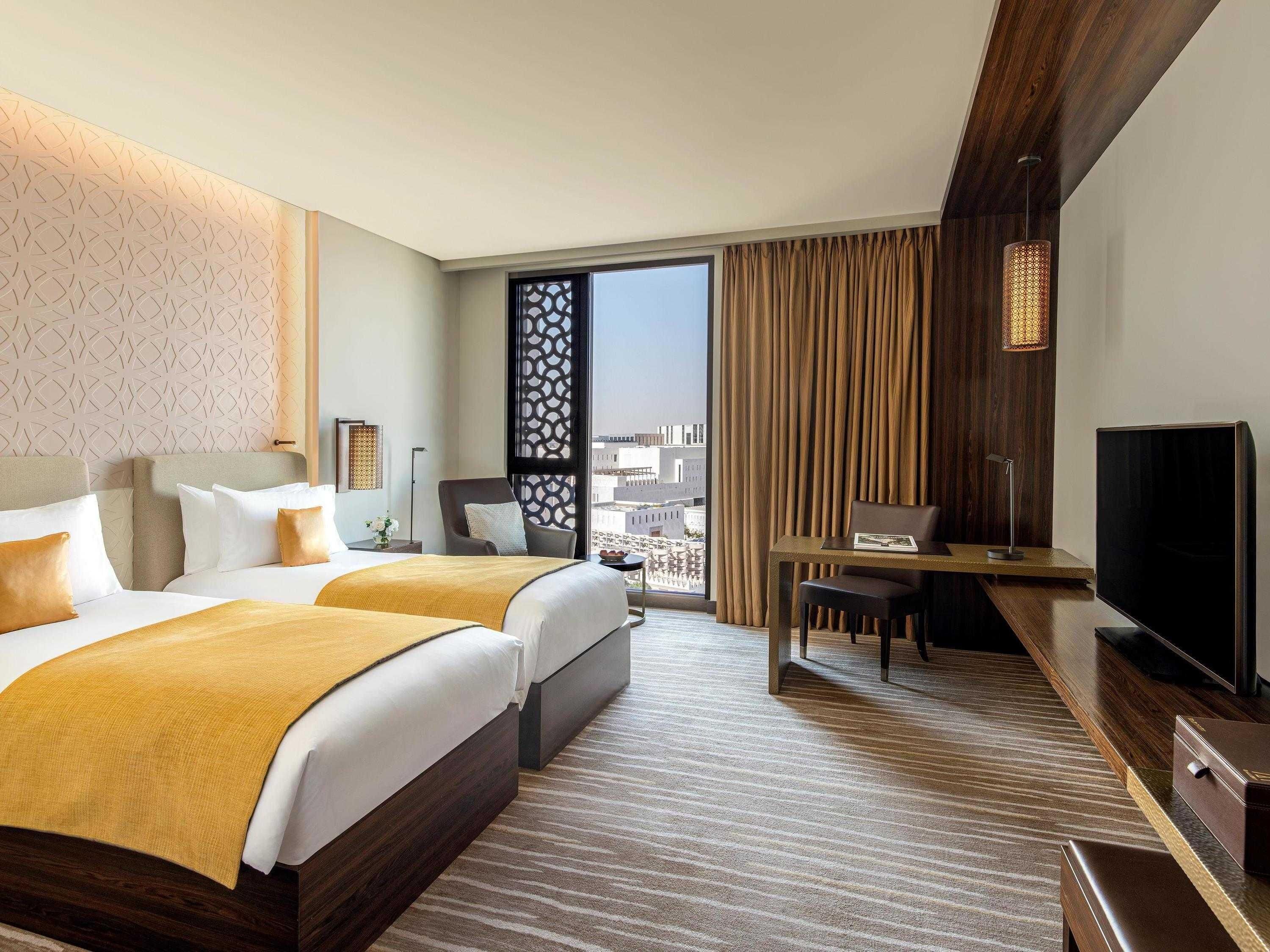 Habitación de hotel con dos camas, un escritorio, un televisor y vistas a la ciudad.