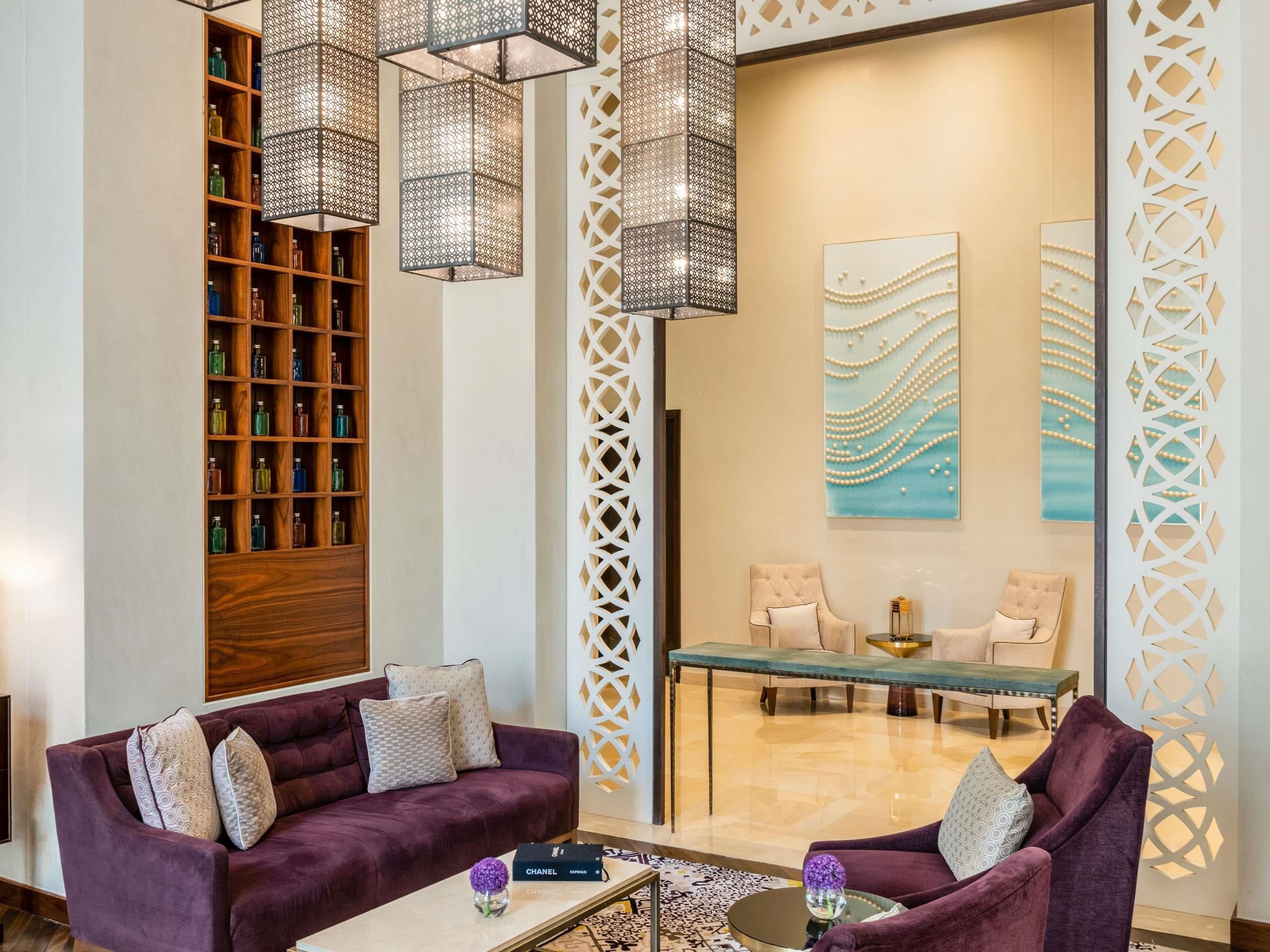 Een moderne lobby met paarse banken, een houten boekenkast, decoratieve wandpanelen en hanglampen.