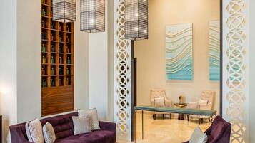 Een moderne lobby met paarse banken, een houten boekenkast, decoratieve wandpanelen en hanglampen.