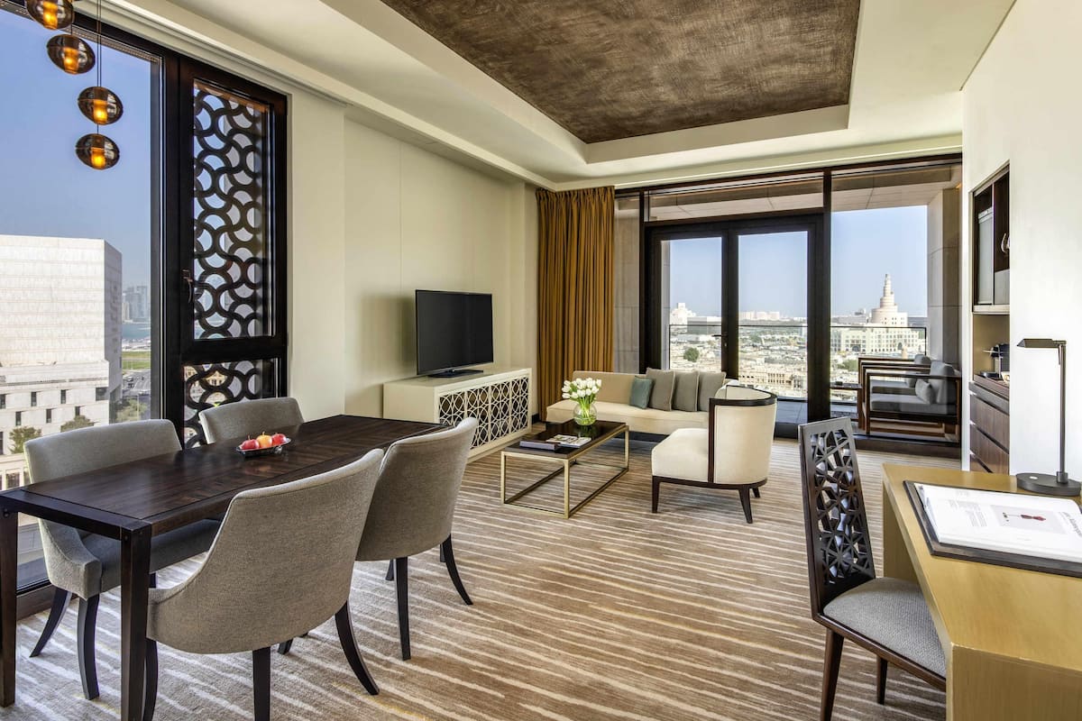 Une chambre dâhĂŽtel moderne dotĂ©e dâun coin repas, dâun canapĂ©, dâune tĂ©lĂ©vision et dâune grande fenĂȘtre offrant une vue sur la ville.