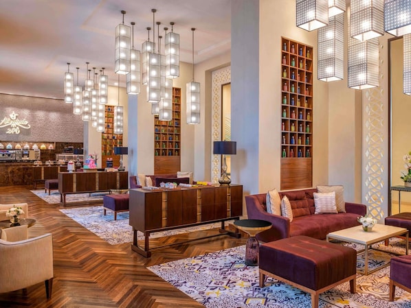 Un hall de hotel con una recepción, zonas de estar y una estantería llena de libros.