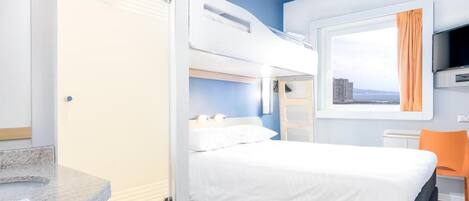 Une chambre d’hôtel avec un lit superposé, un lit simple, une salle de bain avec un lavabo et une fenêtre donnant sur la ville.