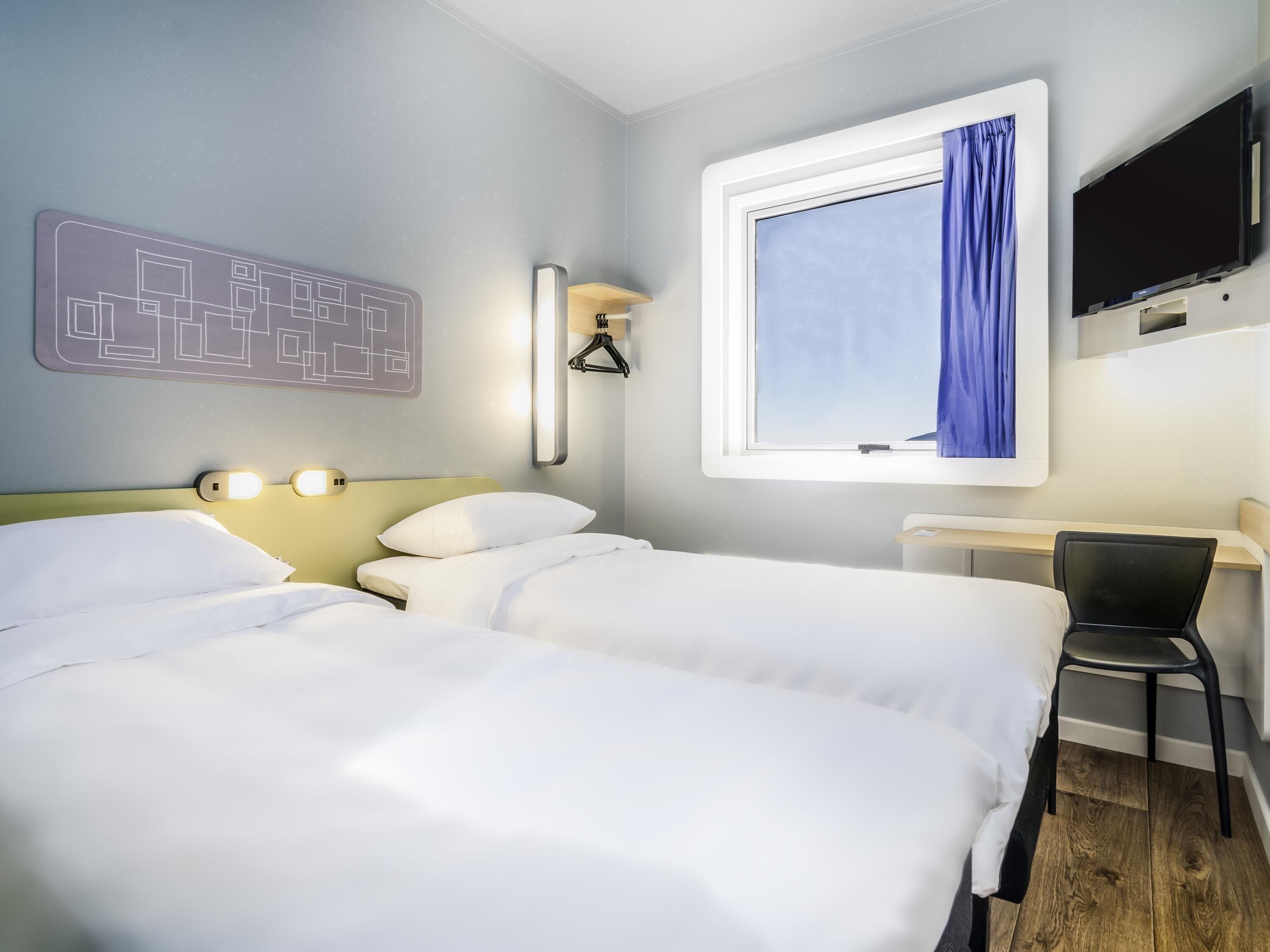 Habitación de hotel con dos camas, un escritorio, una silla, un televisor y una ventana con cortina.
