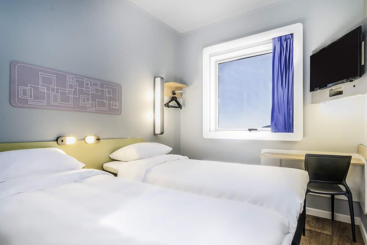 Habitación de hotel con dos camas, un escritorio, una silla, un televisor y una ventana con cortina.