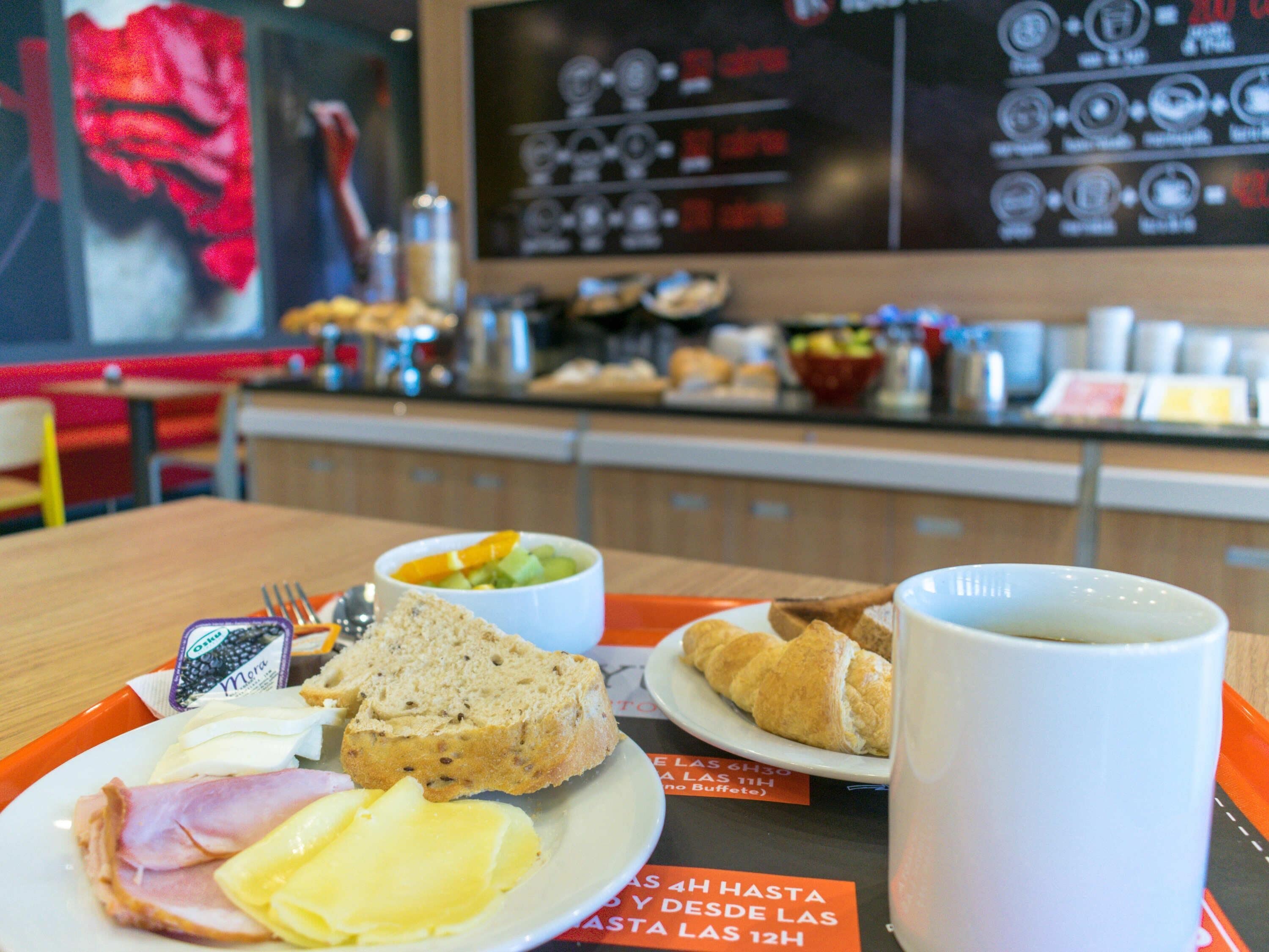 A breakfast tray with ham, cheese, bread, a croissant, and a mug on a table in a restaurant.