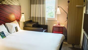 Habitación de hotel con cama, escritorio, silla, ventana con cortinas y lámpara.