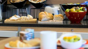 A kitchen counter with bread, a coffee maker, and bowls of fruits.