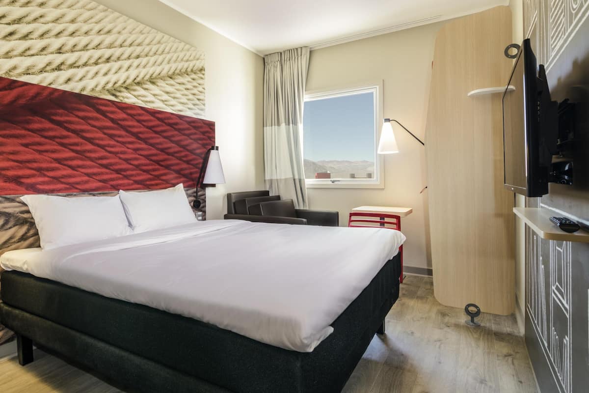 A hotel room with a bed, a desk, a TV, a window with a view, and a wall with a textured design.