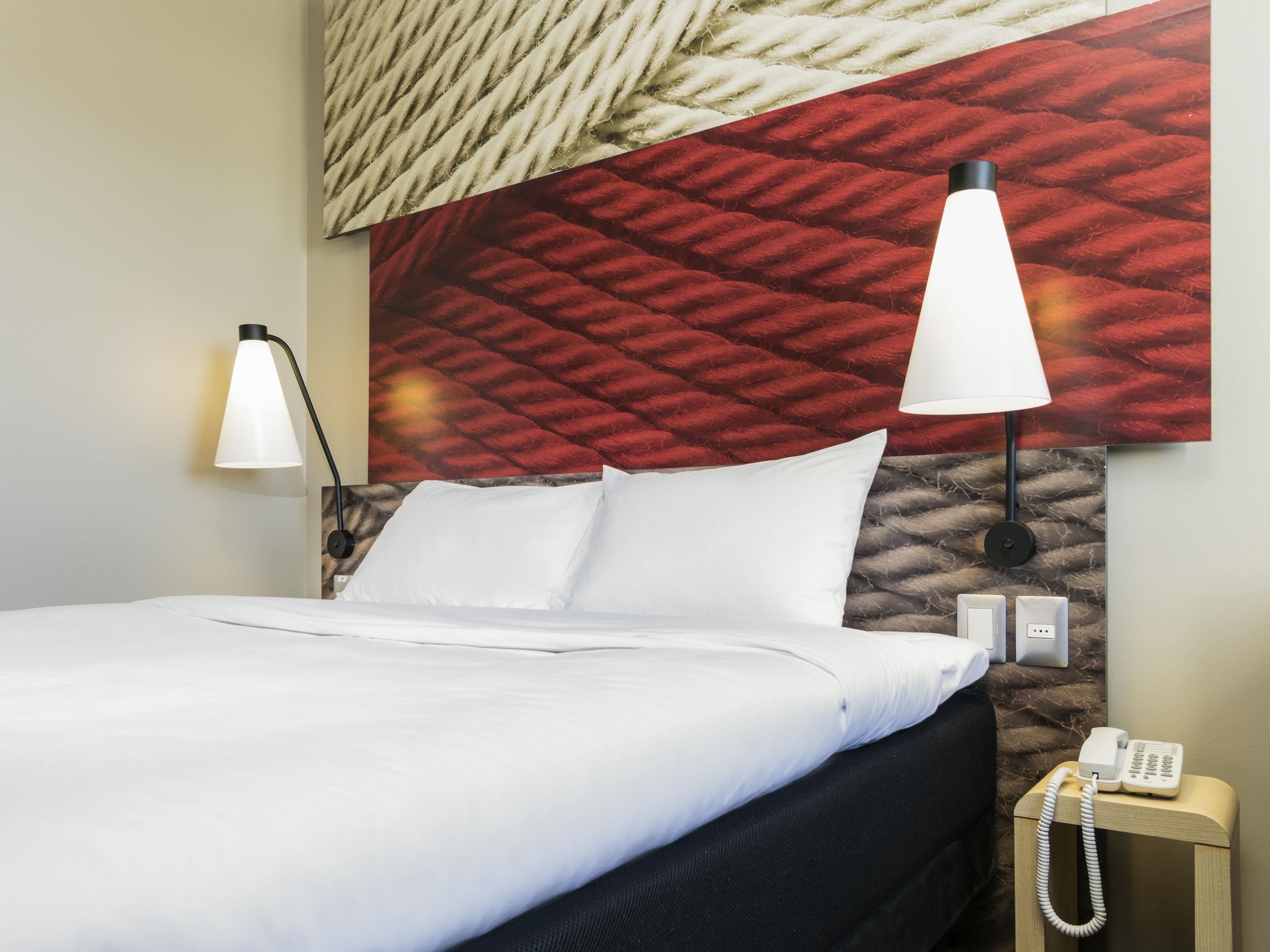 Una habitación de hotel con una cama, dos lámparas de noche, un teléfono y una pared texturizada detrás de la cama.