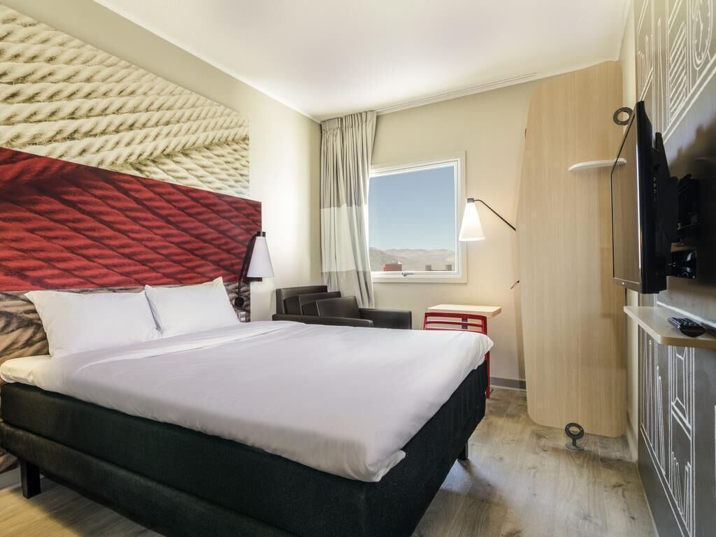 A hotel room with a bed, a desk, a TV, and a window with a view.
