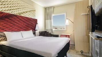 A hotel room with a bed, a desk, a TV, and a window with a view.