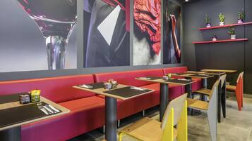 Un intérieur de restaurant moderne avec des sièges rouges, de nombreuses tables et des œuvres d’art murales.