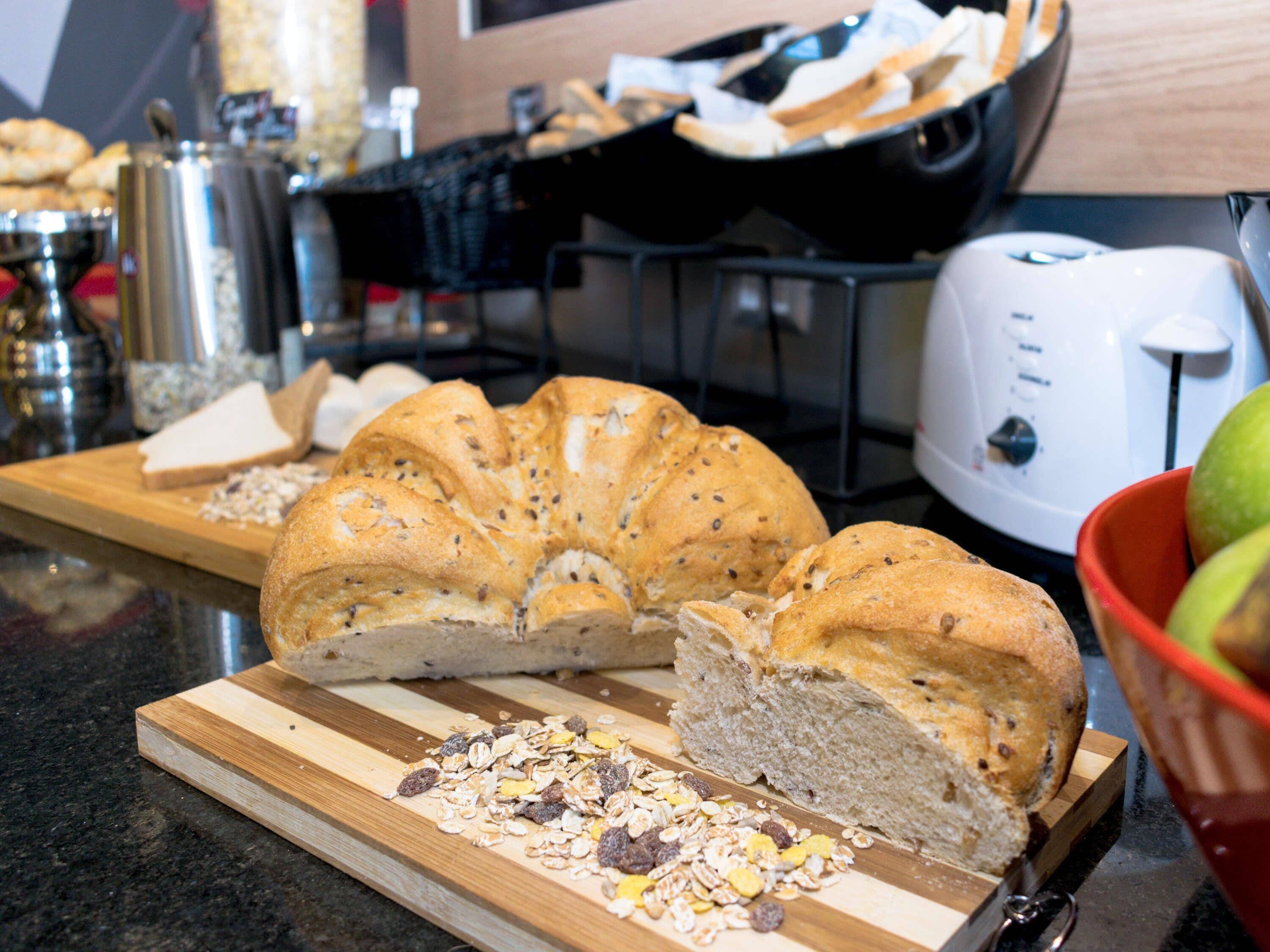 A kitchen counter with a loaf of bread, a cutting board, and a bowl of fruits.
