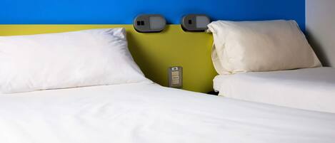 Habitación de hotel con cama, dos almohadas, mesita de noche y toma de corriente.