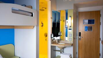Habitación de hotel con una cama, baño con pared amarilla, lavabo y puerta.
