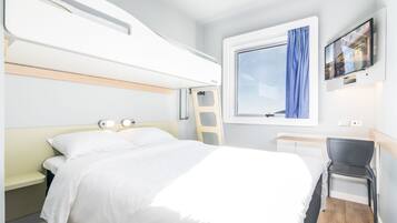 A modern hotel room with a bunk bed, a desk, a chair, a TV, and a window with curtains.