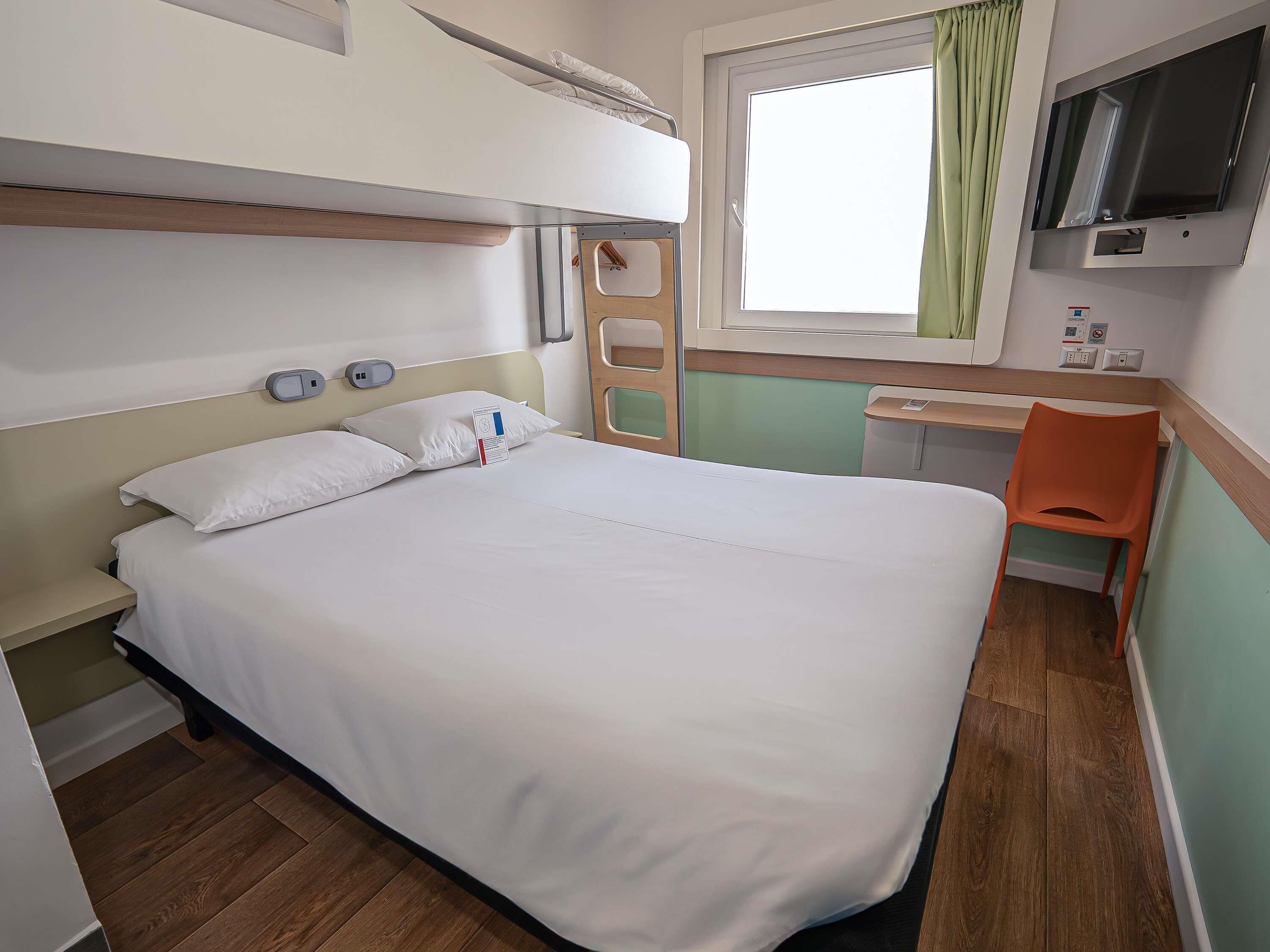 Una habitación de hotel con cama, escritorio, televisor y ventana con cortinas.