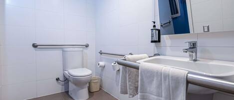 A modern bathroom with a toilet, bidet, hand dryer, and a sink with a mirror.
