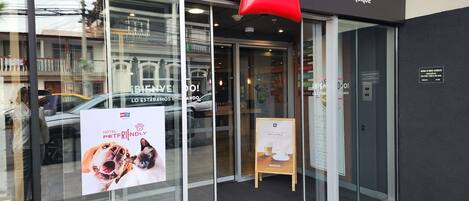 Entrada de un hotel con un letrero rojo de 'ibis', puertas de vidrio y un cartel que indica 'Hotel Friendly Pet'.