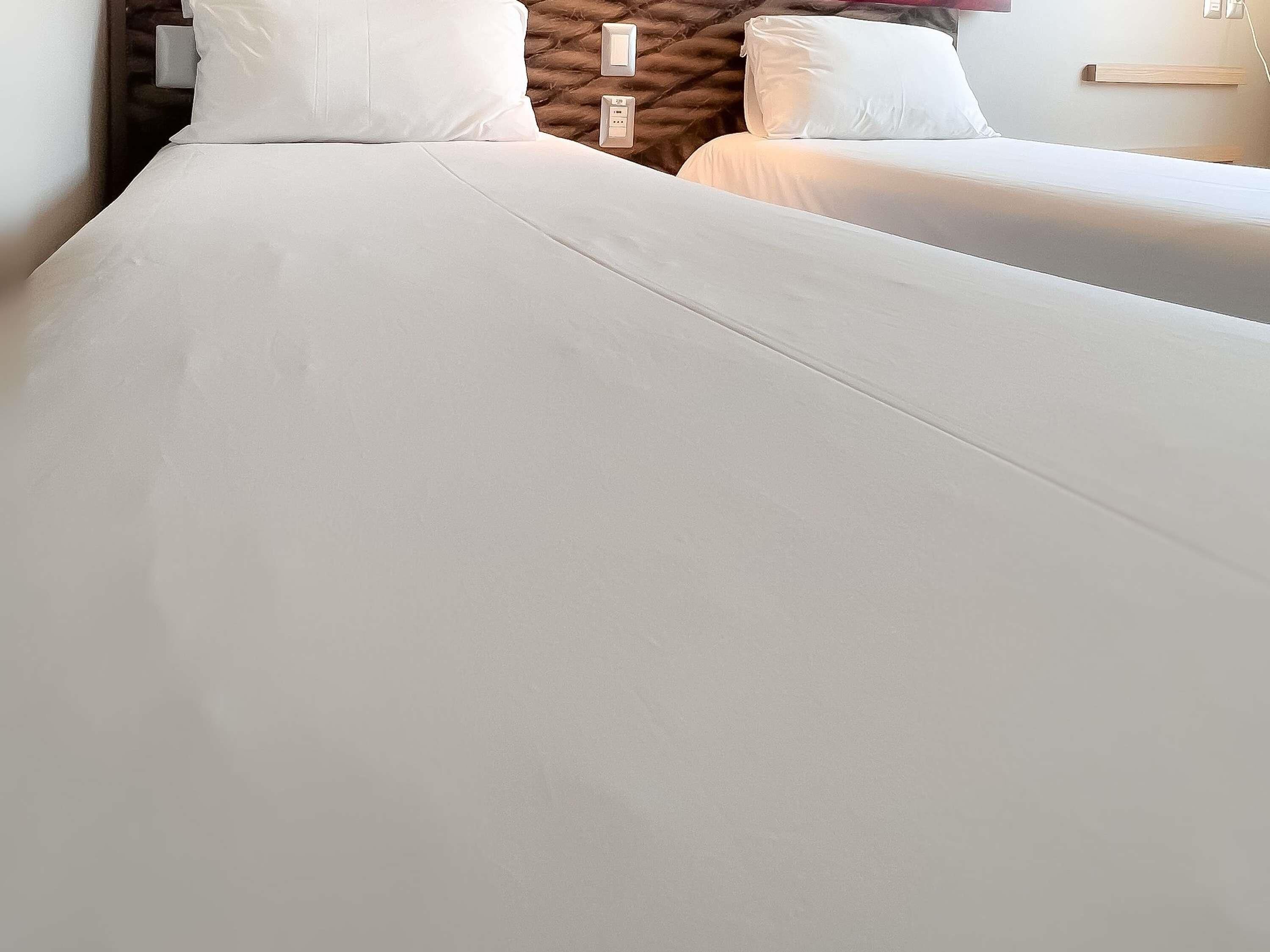 A hotel room with two beds, each with white linens. There are wall sockets and a wooden shelf above the beds.