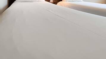 A hotel room with two beds, each with white linens. There are wall sockets and a wooden shelf above the beds.