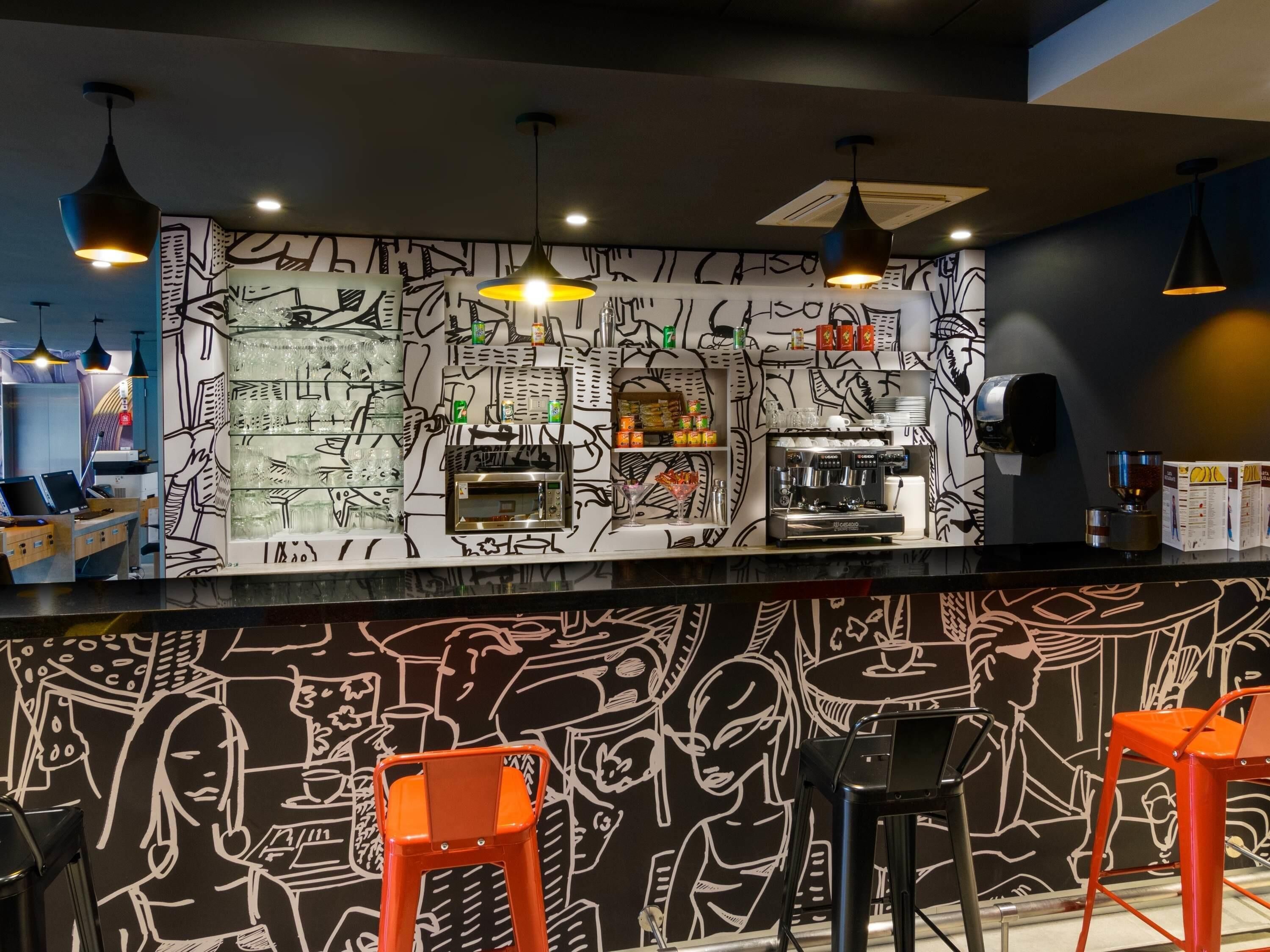 A bar area with a black and white mural, a coffee machine, and orange bar stools.
