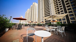 An outdoor patio area with tables and chairs, umbrellas, and potted plants.