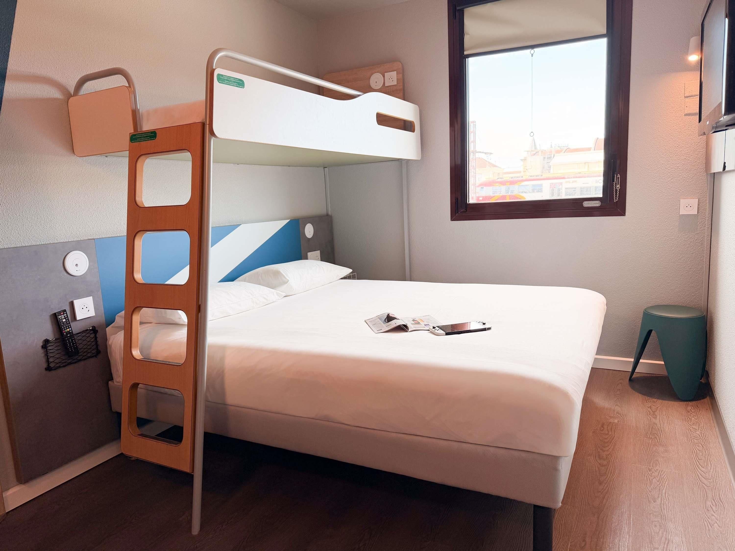 Un letto a castello con una scala, un comodino con un telecomando, una finestra con vista e un piccolo sgabello.