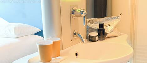 Un baño de hotel con lavabo, espejo y artículos de aseo.