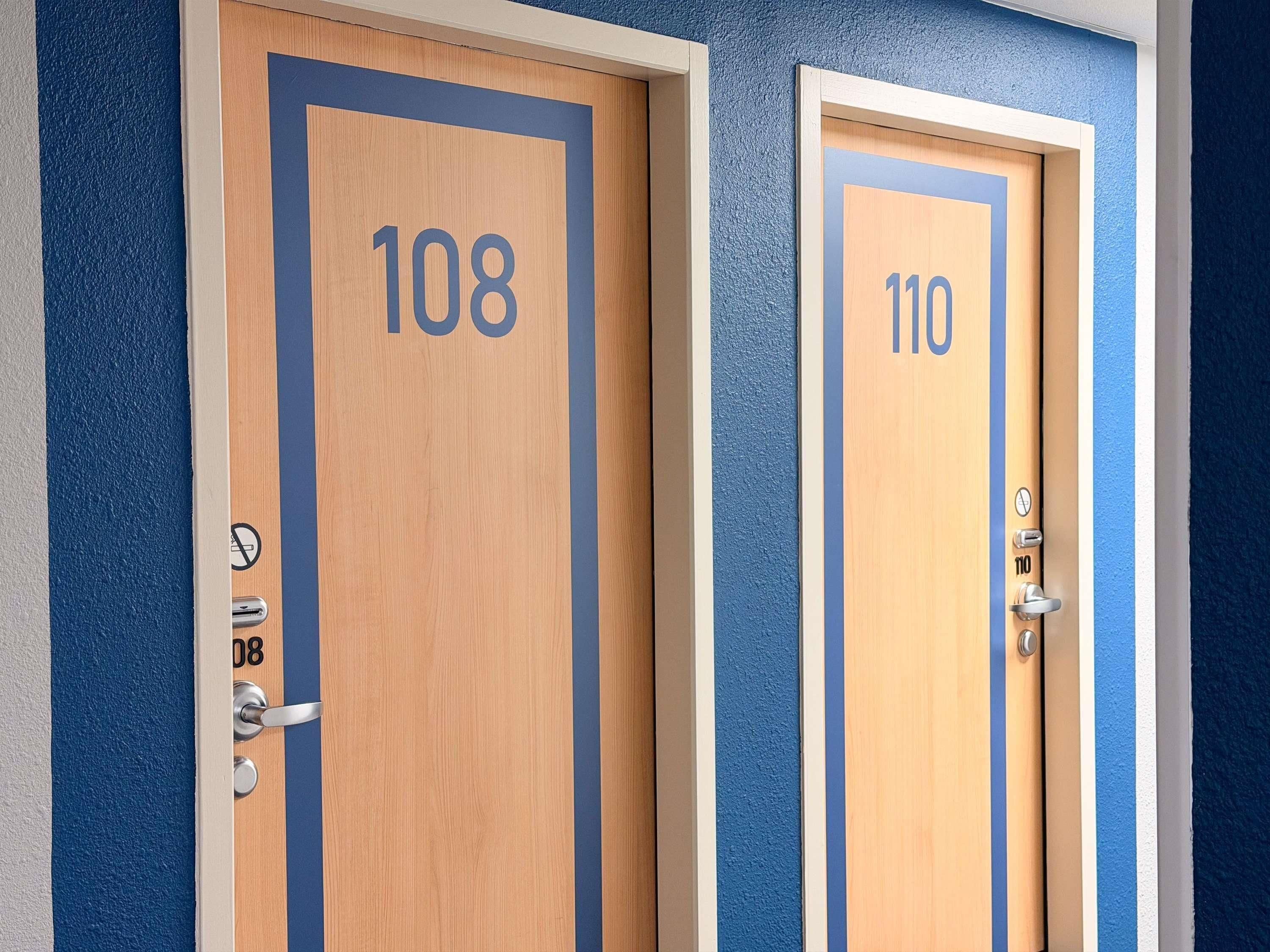 Deux portes en bois, portant les numéros 108 et 110, chacune munie d’un trou de serrure et d’une poignée de porte.