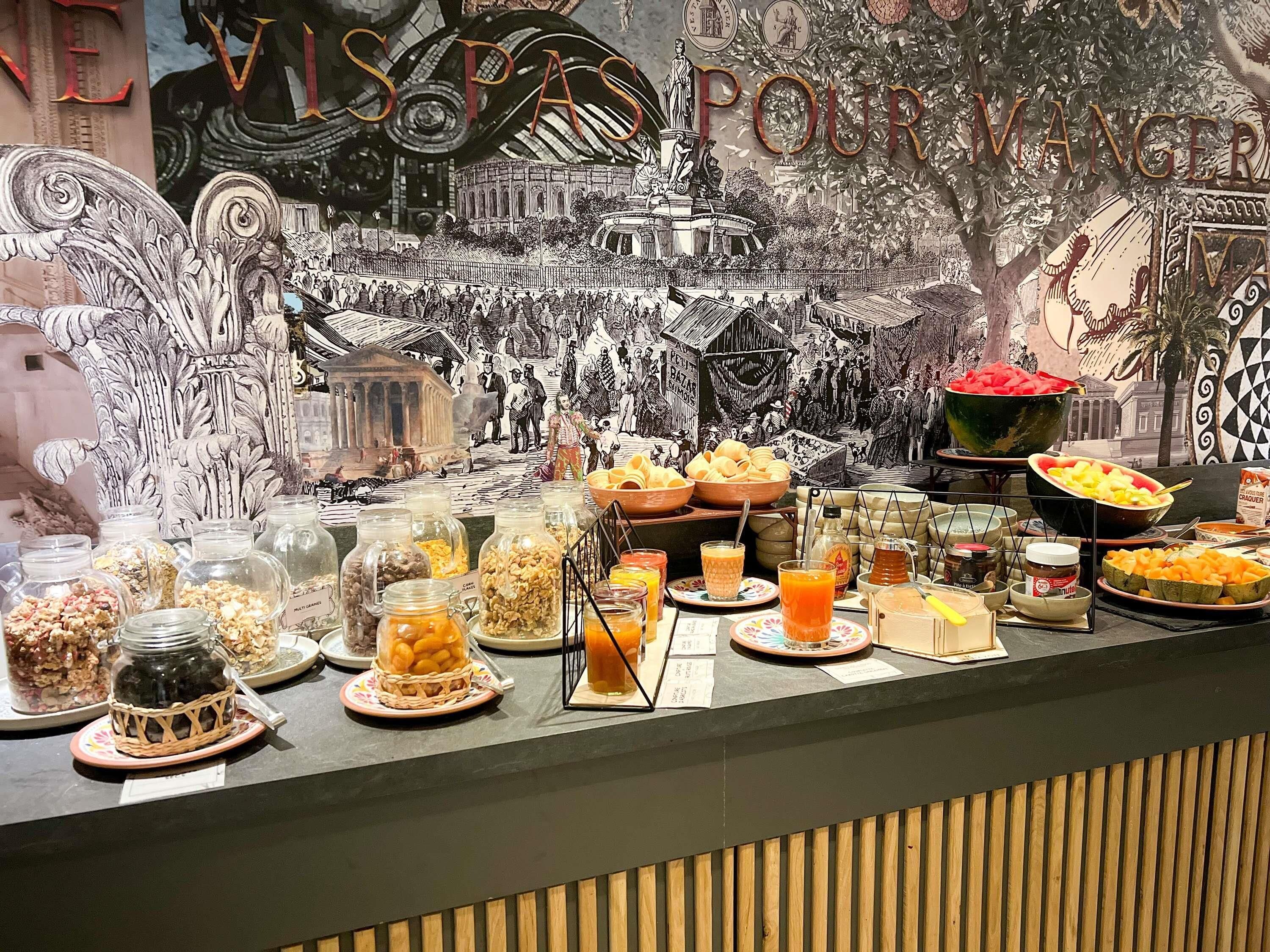Un bufé de desayuno con diversos alimentos y bebidas, con un mural detallado de fondo.