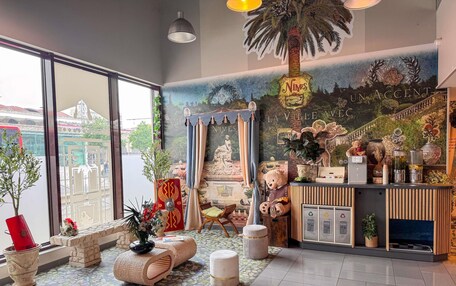 A hotel lobby with large windows, a reception desk, a mural, and a decorative palm tree.