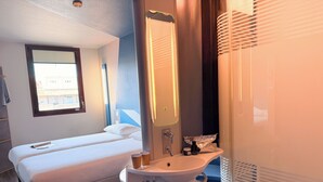 Une chambre d’hôtel avec un lit, une table de chevet avec une lampe, un miroir, un lavabo et une fenêtre.