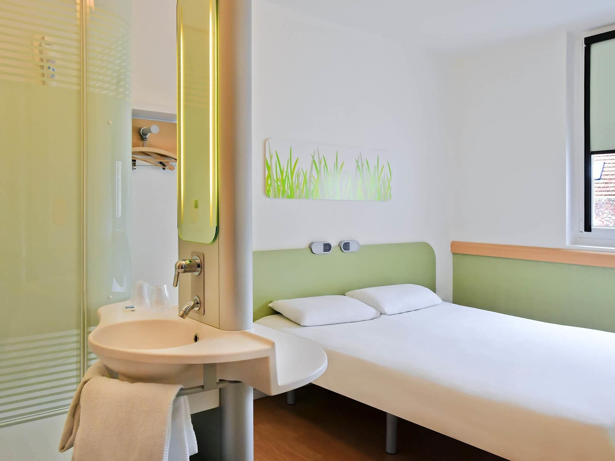 Une chambre d’hôtel avec un lit, une table de chevet, un lavabo et un miroir.